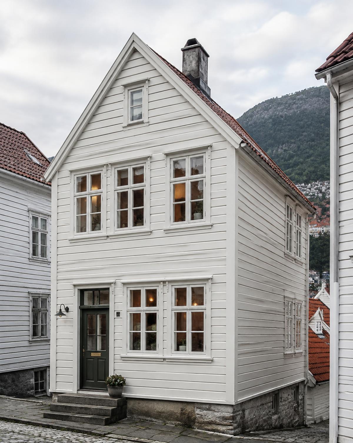 Restaurert hvitt trehus i en brosteinsgate i Bergen